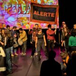 Action sur les planches de la scène principale du théâtre. Plusieurs militant-es montent sur scène. Certain-es tiennent une banderole "ALERTE".