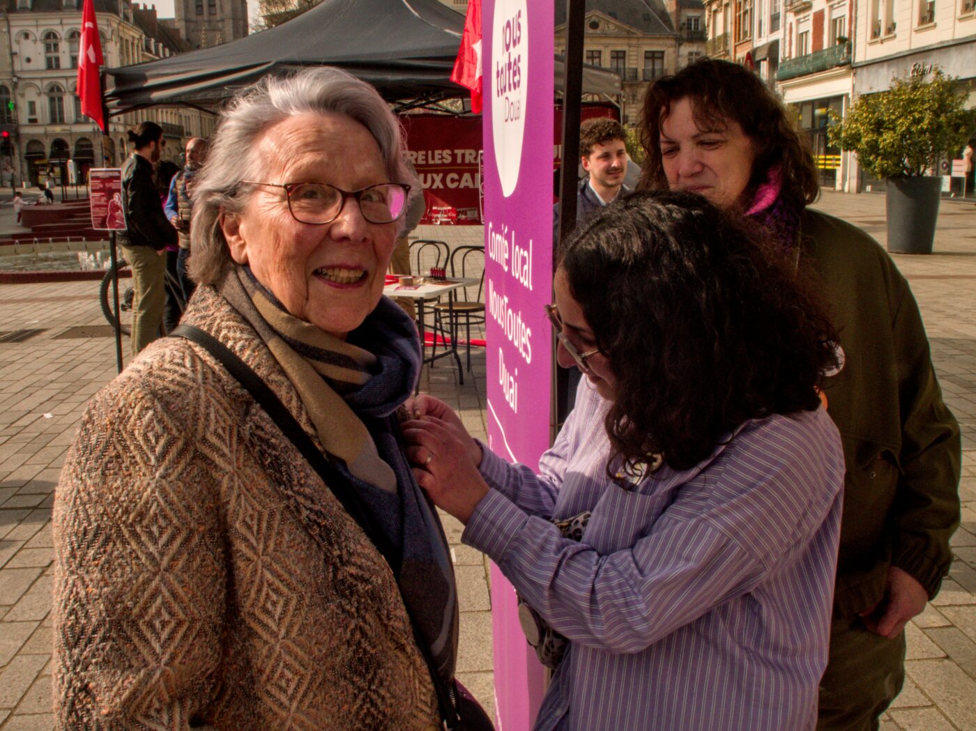 Une jeune militante de Nous Toutes accroche un badge à la veste d'une militante communiste âgée.