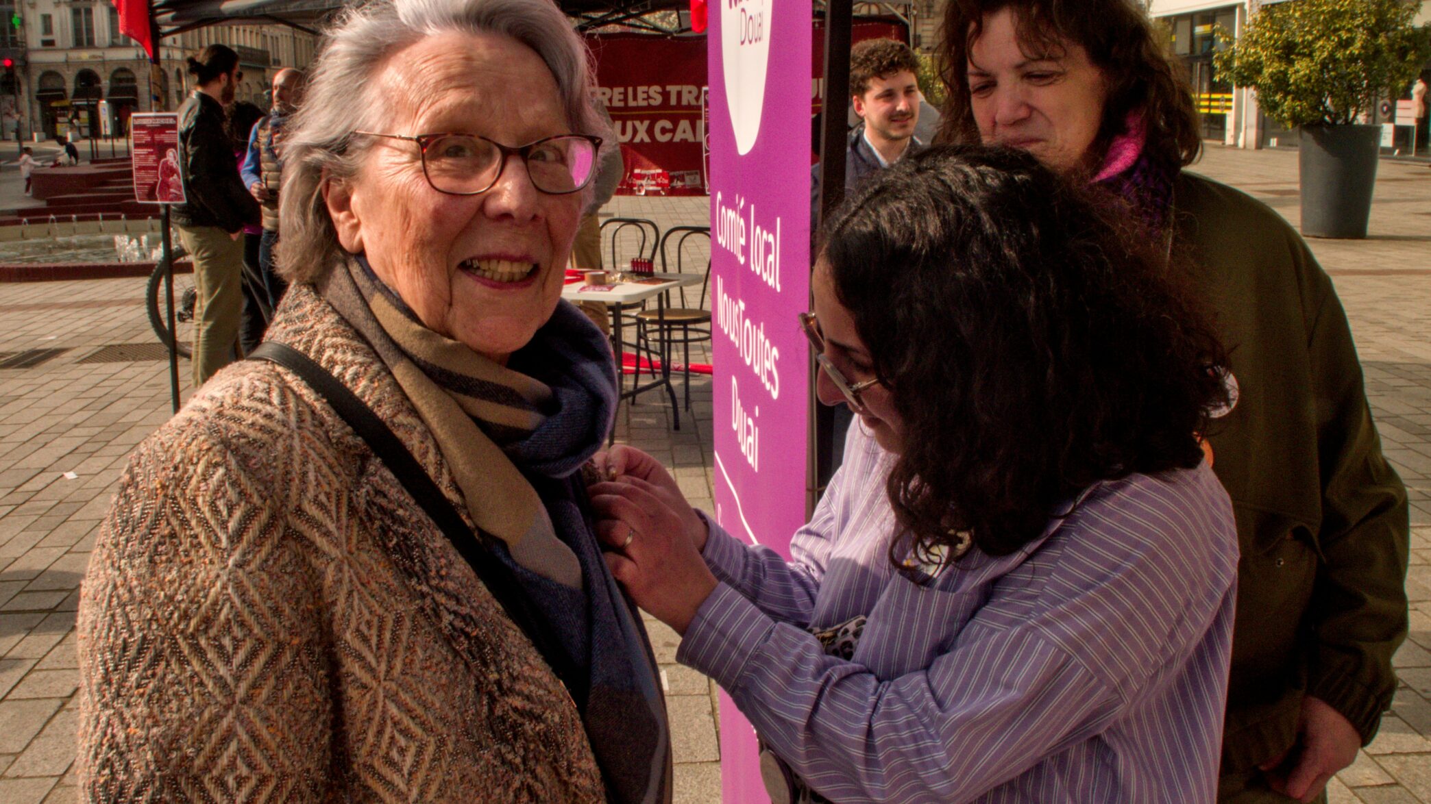 Une jeune militante de Nous Toutes accroche un badge à la veste d'une militante communiste âgée.