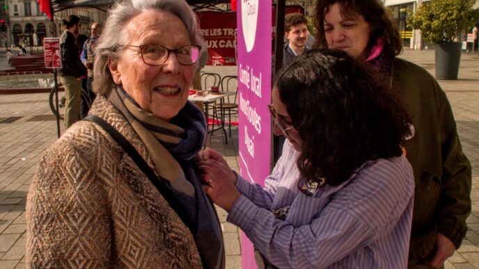 Une jeune militante de Nous Toutes accroche un badge à la veste d'une militante communiste âgée.