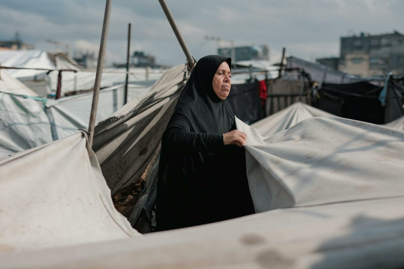 Une femme du Moyen-Orient entretient des tentes dans un camp de Gaza, symbolisant la résilience au milieu du conflit.