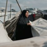 Une femme du Moyen-Orient entretient des tentes dans un camp de Gaza, symbolisant la résilience au milieu du conflit.