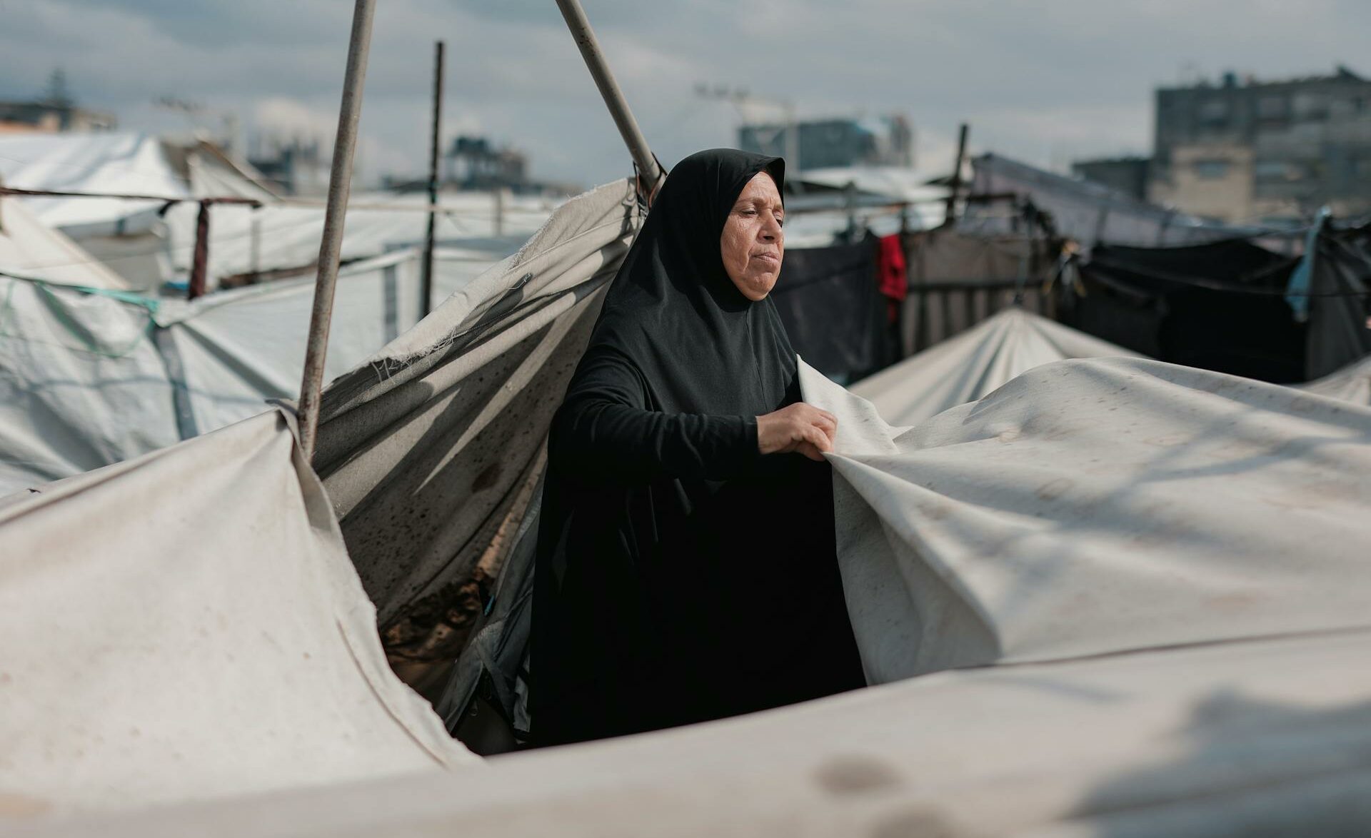 Une femme du Moyen-Orient entretient des tentes dans un camp de Gaza, symbolisant la résilience au milieu du conflit.