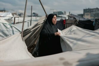 Une femme du Moyen-Orient entretient des tentes dans un camp de Gaza, symbolisant la résilience au milieu du conflit.