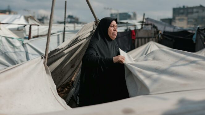 Une femme du Moyen-Orient entretient des tentes dans un camp de Gaza, symbolisant la résilience au milieu du conflit.