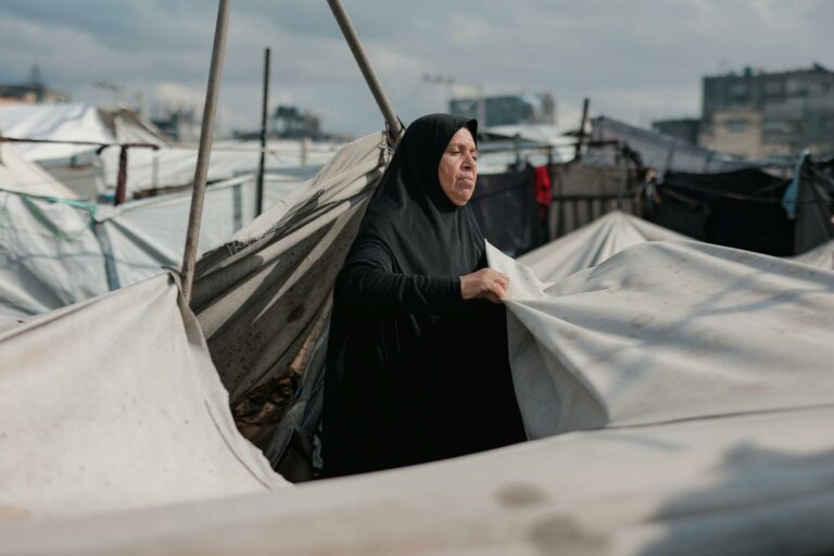 Une femme du Moyen-Orient entretient des tentes dans un camp de Gaza, symbolisant la résilience au milieu du conflit.
