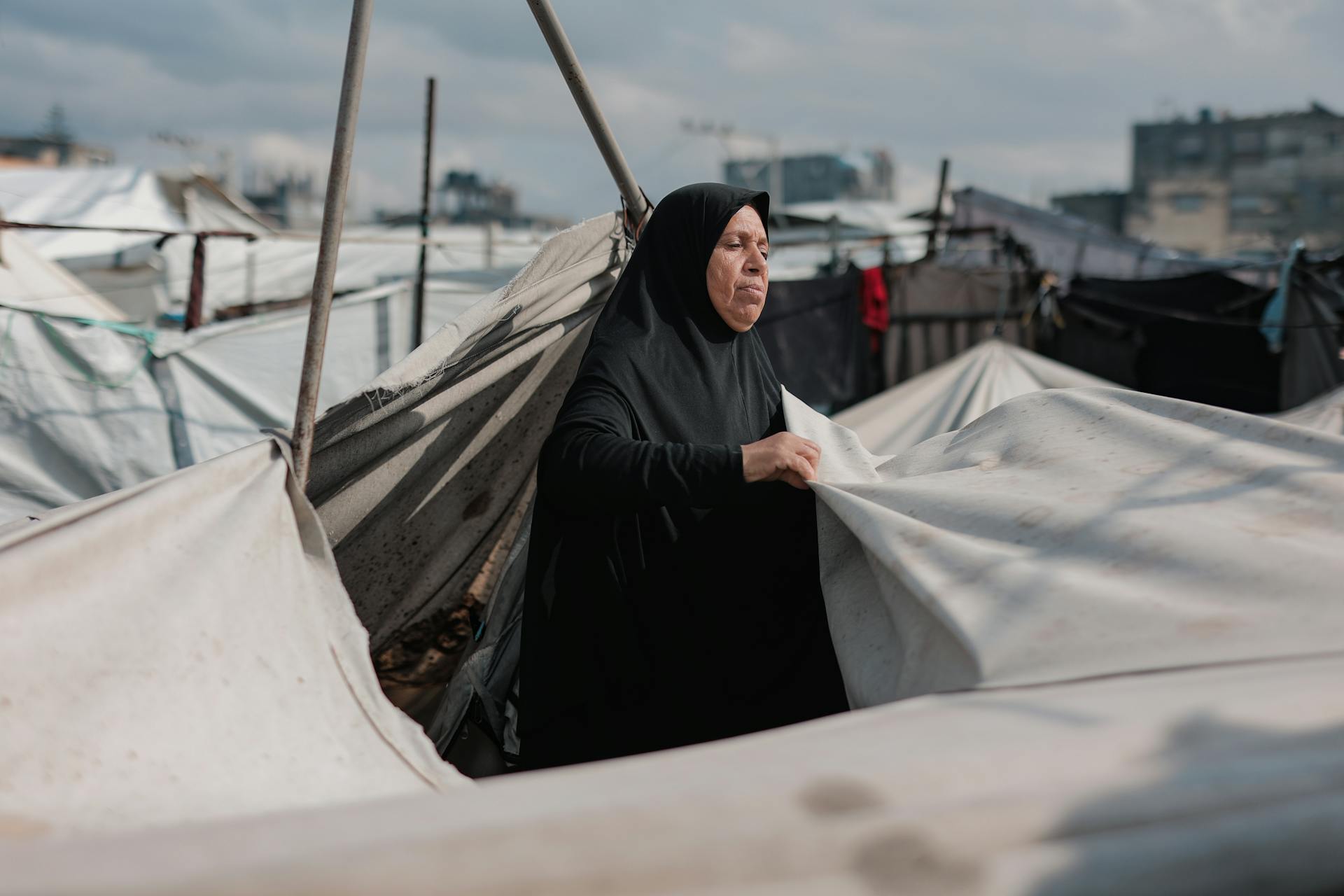 Une femme du Moyen-Orient entretient des tentes dans un camp de Gaza, symbolisant la résilience au milieu du conflit.